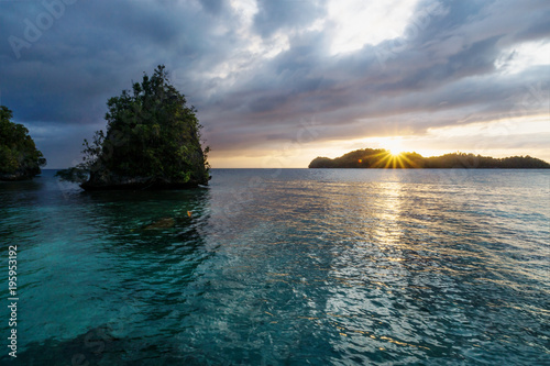 Sunset with blue water and stone with green bushes at Kadidiri, Togian Islands, Indonesia, Asia