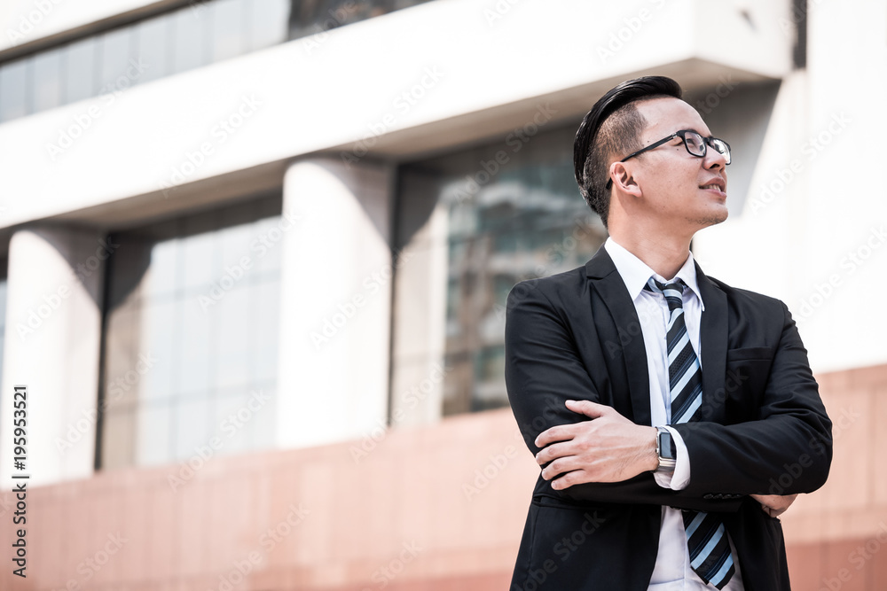 Portrait of young Asian businessman in black suit standing with office building background. Free space for text Portrait of young Asian businessman in black suit standing with office building background. Free space for text