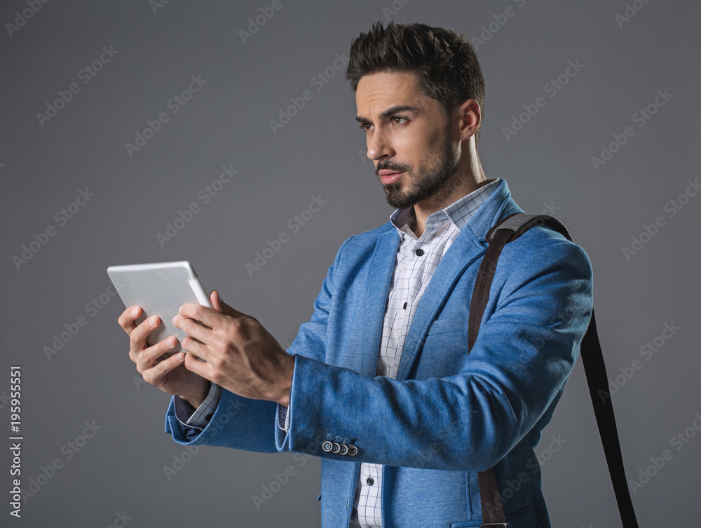 Waist up portrait of thinking businessman with shoulder bag surfing internet on clipboard. Isolated on gray background Waist up portrait of thinking businessman with shoulder bag surfing internet on clipboard. Isolated on gray background