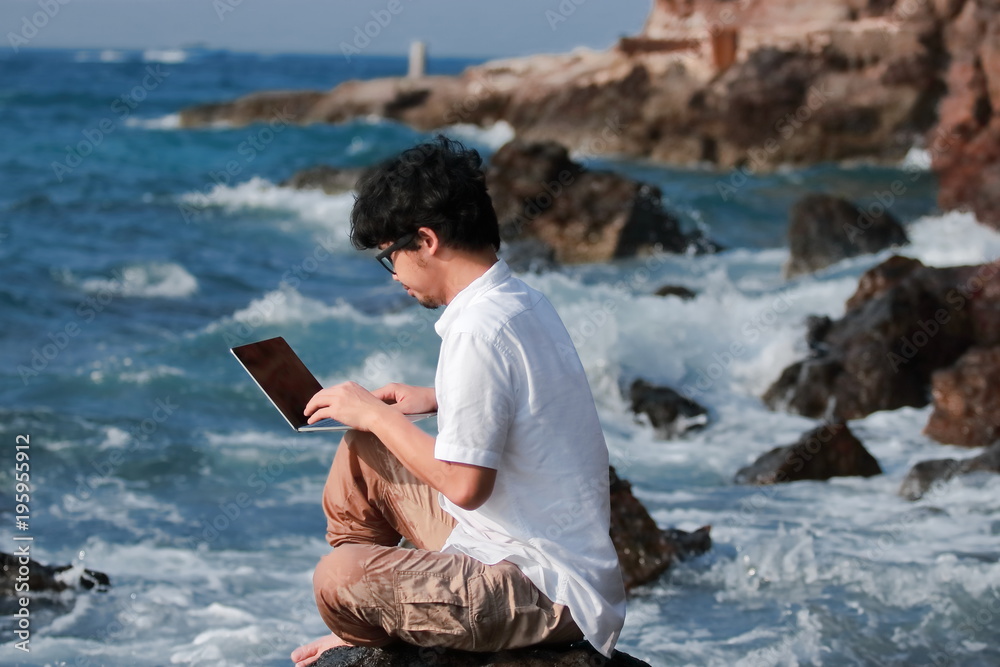 Summer vacation concept. Lifestyle Asian man with laptop relaxing at blue sea shore.