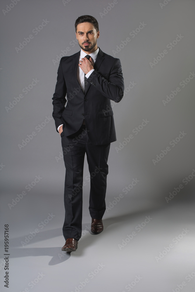 Φωτογραφία Full length portrait of concentrated bearded man in business suit touching up tie