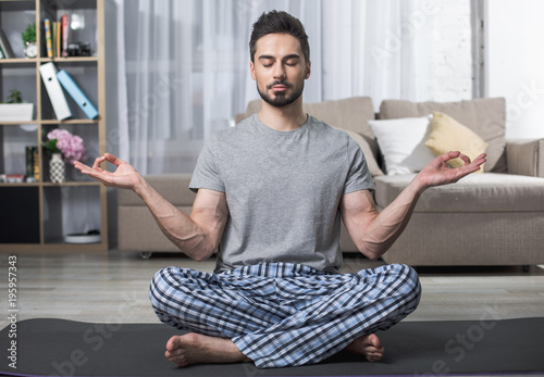 Portrait of calm bearded male sitting on yoga carpet in living room