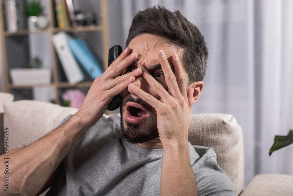 Φωτογραφία Terrified guy in living room sitting on sofa and covering his face with hands in