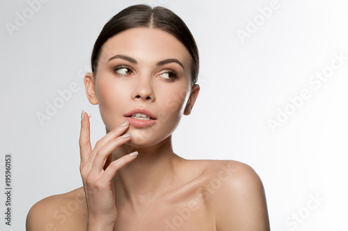 Portrait of serene young woman applying cream on her face. Isolated
