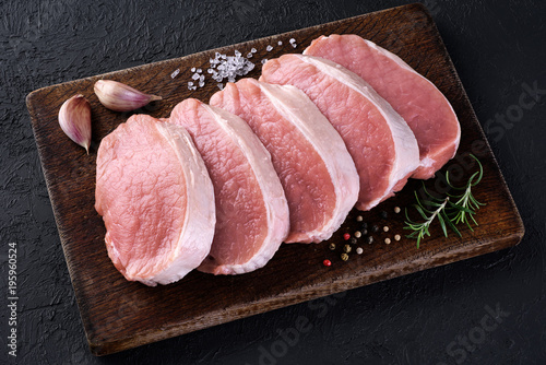 Raw sliced pork loin with salt, pepper, rosemary and garlic on a dark background. Fresh meat.