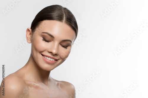 Enjoying skincare treatment. Portrait of cheerful young woman laughing while posing with bare shoulders. Her eyes are closed with pleasure. Isolated and copy space