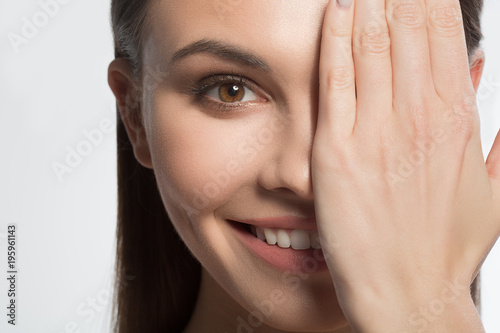 Close up of excited girl showing her perfect skin. She is covering half of face by palm and smiling. Isolated