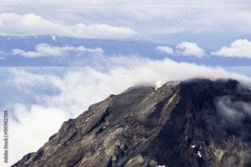 An aerial view of an Alaskan peak surrounded by smoky clouds and a blue sky. Scenic mountain in Alaska. Concept for achievement, goal and solitude