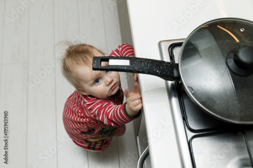 child safety at home concept - toddler reaching for pan on the stove in kitchen photo