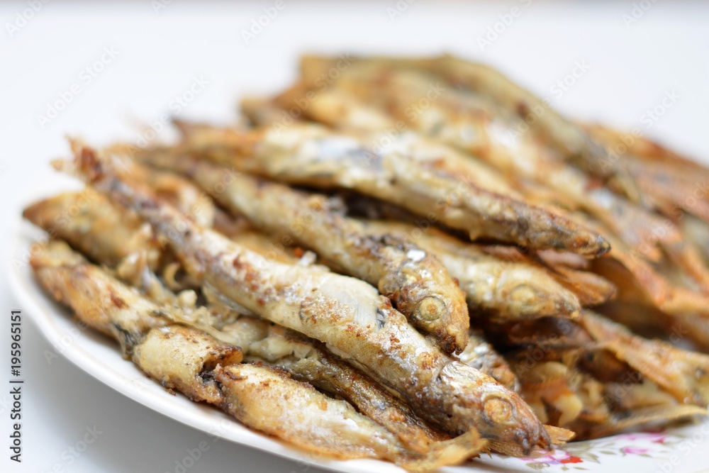 Fried smelt in a frying pan on the table with spices, lime and thyme. Small crispy fish. Selective focus