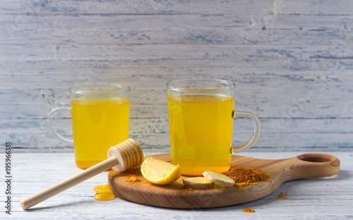 Two glasses of energy tonic healthy drink with turmeric, ginger, lemon and honey on a wooden board, selective focus