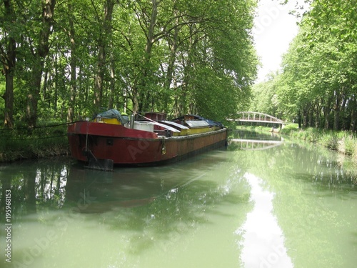 Southern France, side canal of the Garonne river, ( called  Canal lateral a la Garonne ) view of straight canal section with bridge , vessel and trees on the banks