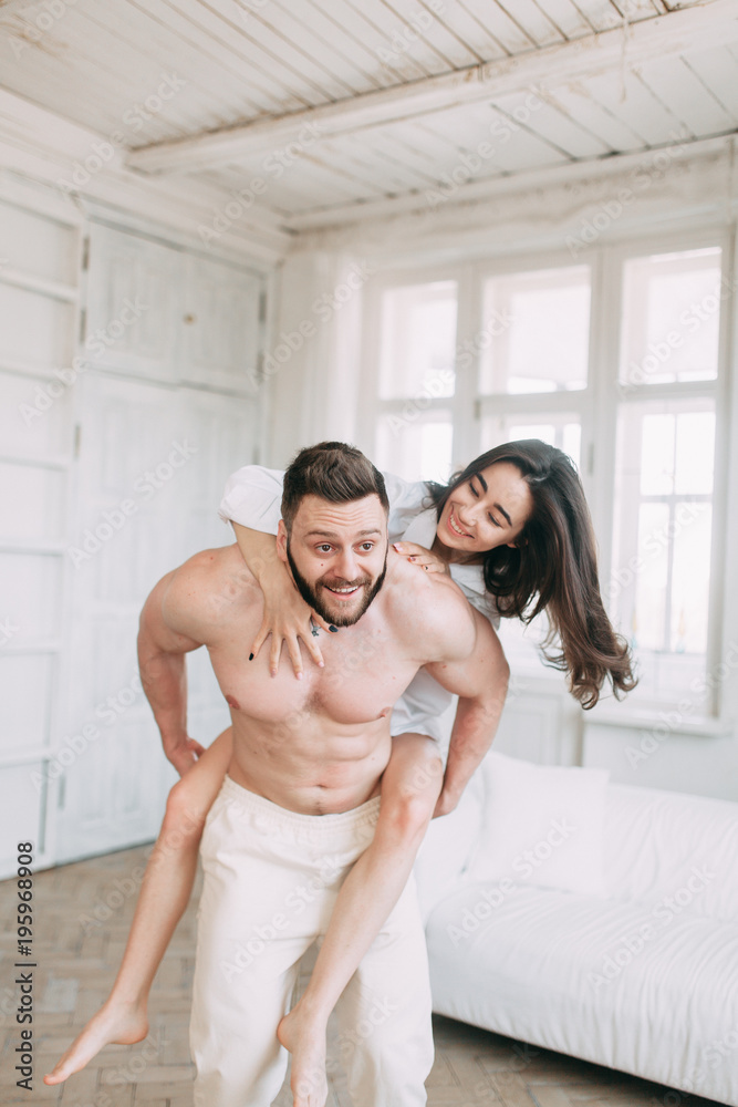 Young happy couple at home, cuddling, and kissing are. Beautiful Sunny morning with your loved ones in pajamas mad and laugh. Young happy couple at home, cuddling, and kissing are. Beautiful Sunny morning with your loved ones in pajamas mad and laugh.