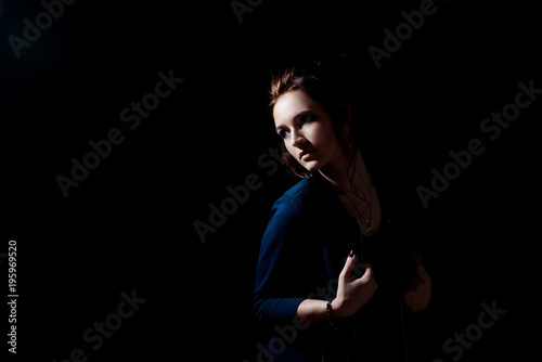 A girl in the fashion style holds hands over her jacket and looks away on a black background with space for text