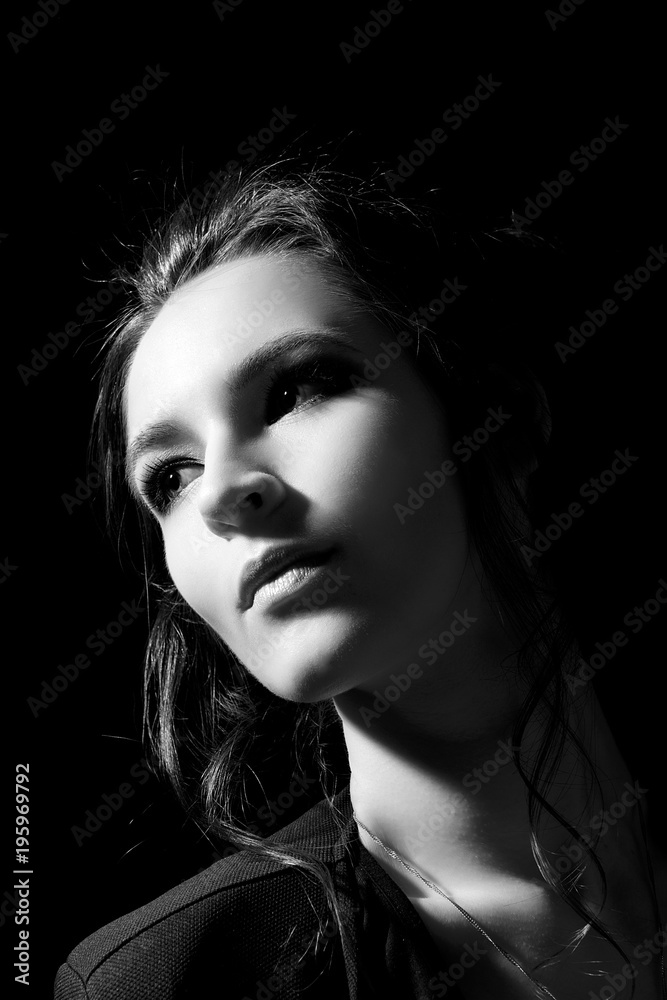 The girl in the fashion style with professional make-up looks to the side on a close-up on a black background in a low key