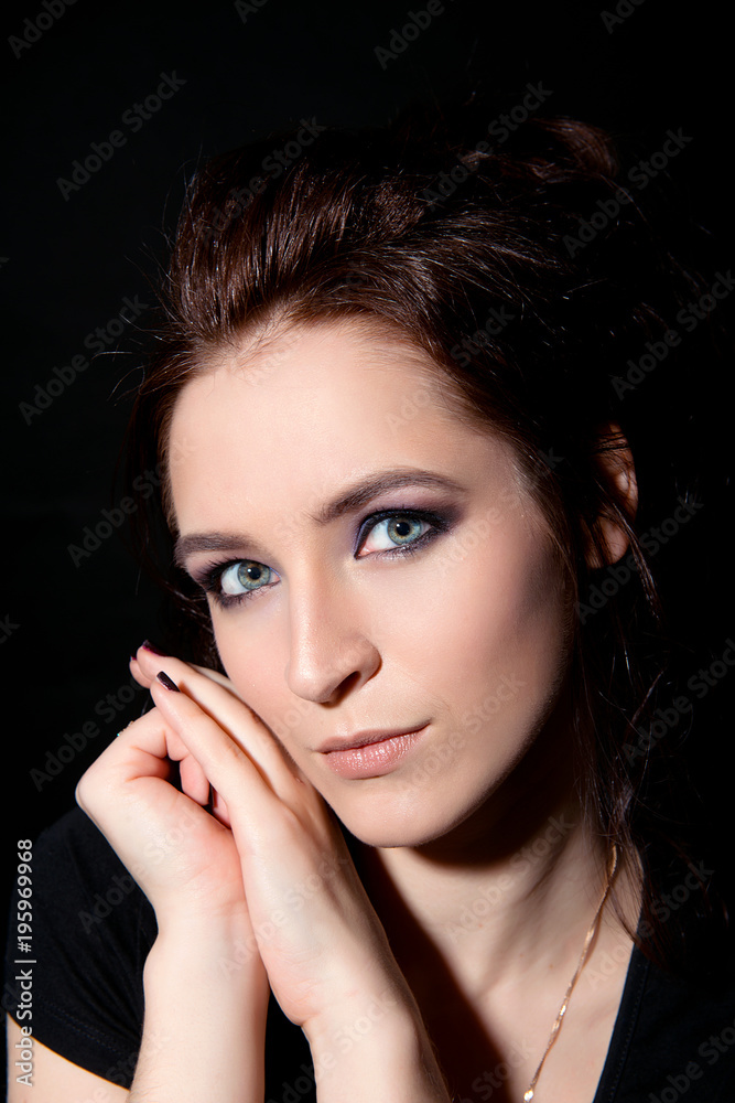 Girl with professional make-up and clean skin leans her hands against her cheek against a black background close-up Girl with professional make-up and clean skin leans her hands against her cheek against a black background close-up
