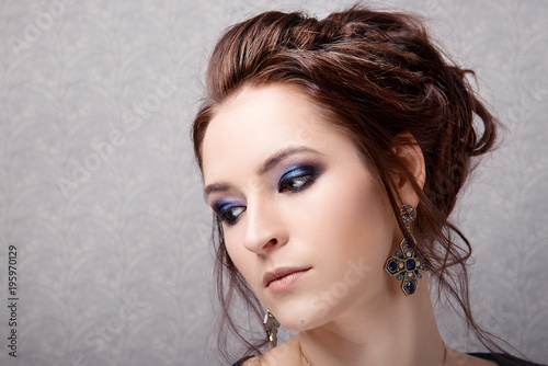 Brunette girl with evening make-up and hairstyle high bun looks toward the close-up on a gray background