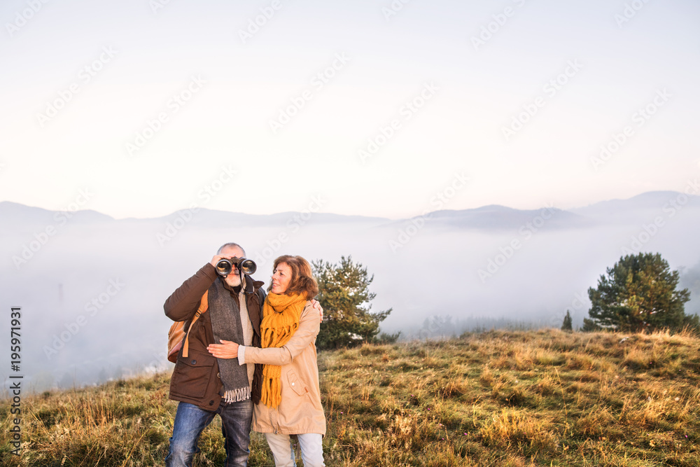 Senior couple with binoculars on a walk in an autumn nature.