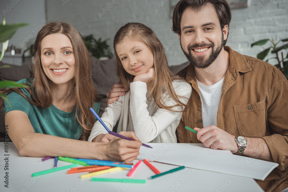 smiling parents and daughter drawing with felt-tip pens and looking at camera smiling parents and daughter drawing with felt-tip pens and looking at camera