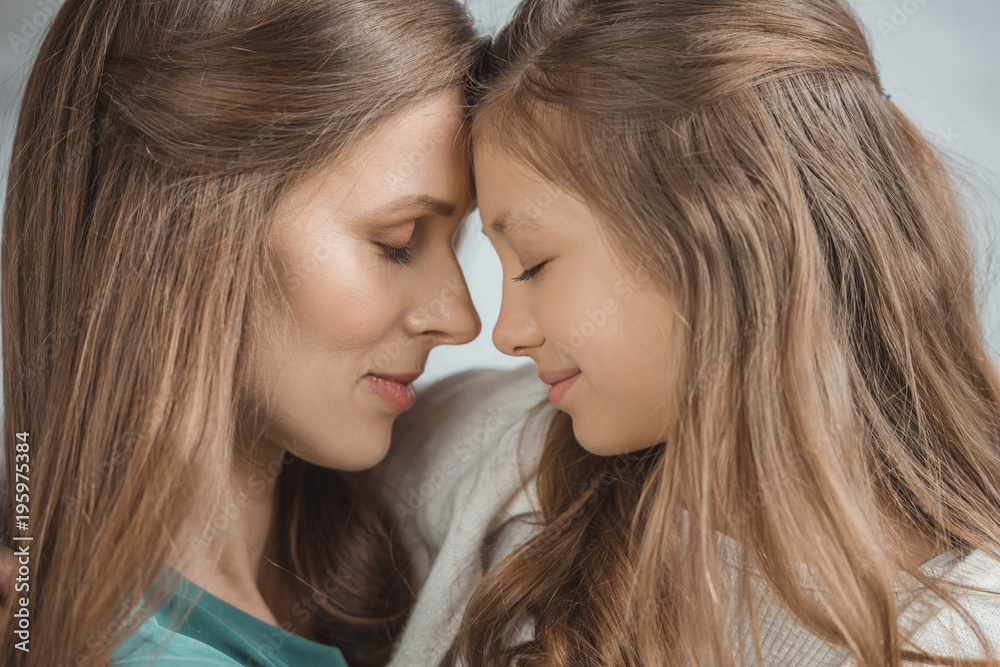 side view of mother and daughter touching with foreheads at home side view of mother and daughter touching with foreheads at home