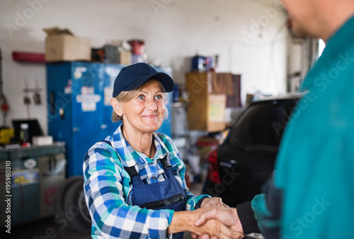 Senior female mechanic repairing a car in a garage.