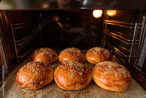 homemade burger rolls sprinkled with sesame seeds are baked in the oven