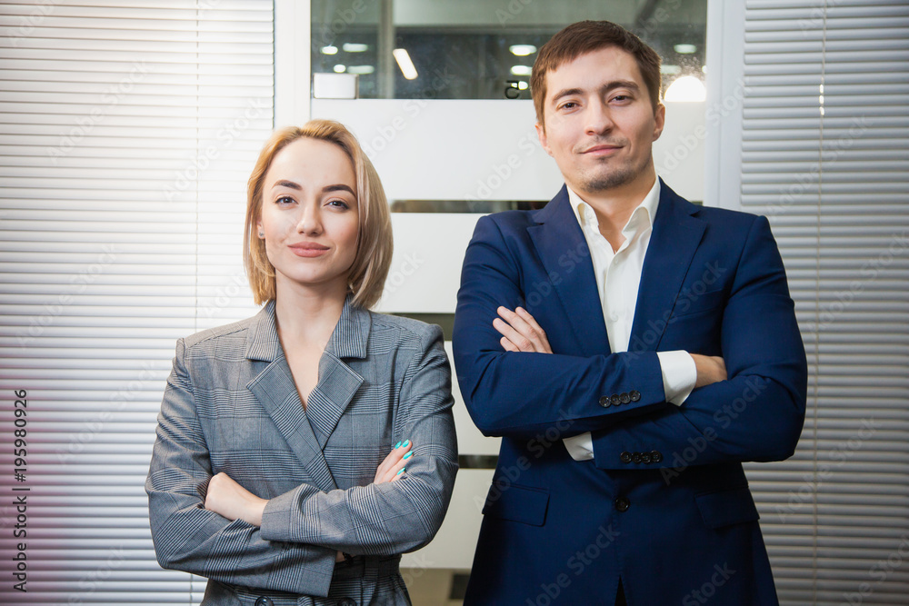 Two respectable business people in formal suits stand together. Man and woman at office room pose to camera. Teamwork, cooperation, success concept Two respectable business people in formal suits stand together. Man and woman at office room pose to camera. Teamwork, cooperation, success concept