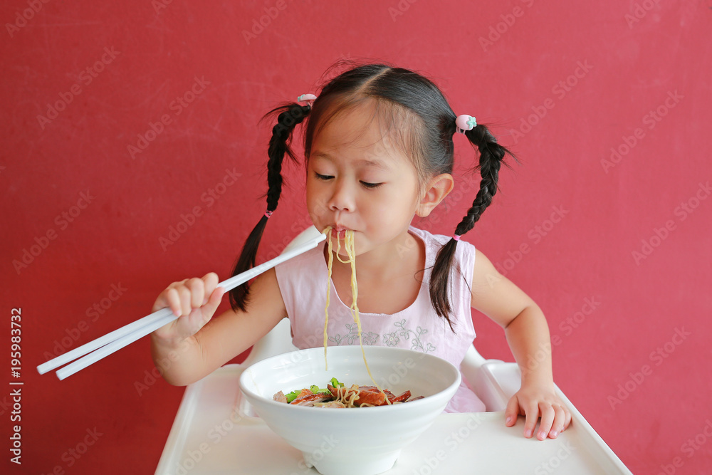 Little asian girl eating Egg noodle with roasted duck and pork on high chair against red wall background.
Little asian girl eating Egg noodle with roasted duck and pork on high chair against red wall background.