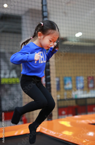Asian kid girl jumping at trampoline in indoors playground. Active girl having fun at sport center on holiday.