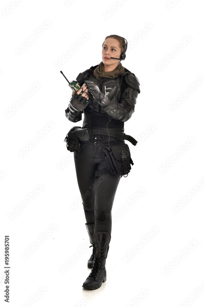 full length portrait of female  soldier wearing black  tactical armour, standing pose holding a walkie talkie, isolated on white studio background.