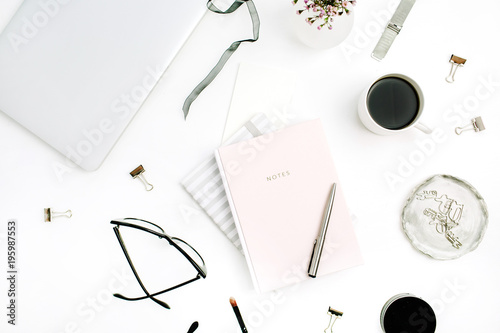 Feminine modern home office desk with pastel pink notebook, glasses, coffee cup, wildflowers and stationery on white background. Flat lay, top view.