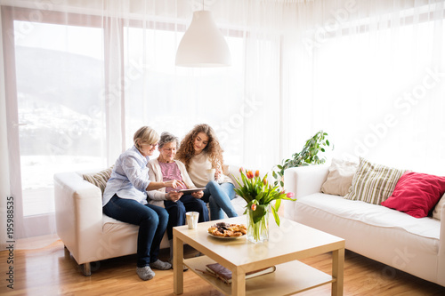 A teenage girl, mother and grandmother with tablet at home.