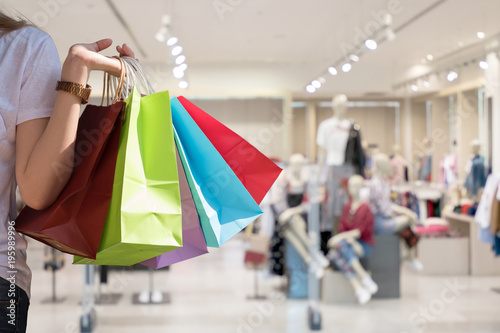Attraction woman hand holding shopping bags in one hand with blur cloth shop background - Shopping Concept