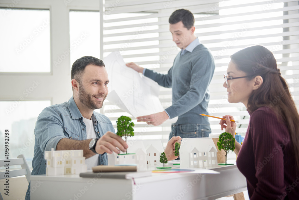 Interesting project. Handsome joyful bearded man smiling and holding a tree miniature while sitting at the table and discussing work Interesting project. Handsome joyful bearded man smiling and holding a tree miniature while sitting at the table and discussing work