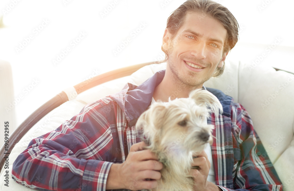 close-up of a smiling guy stroking his dog while sitting in a large armchair. close-up of a smiling guy stroking his dog while sitting in a large armchair.