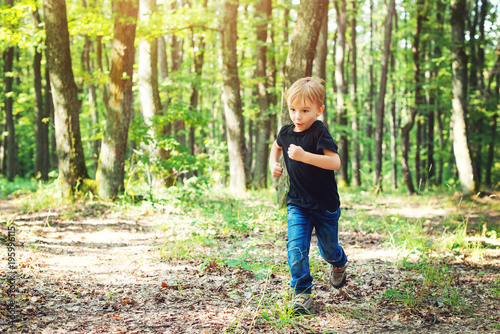 Happy blond boy running in sunny day in forest.
