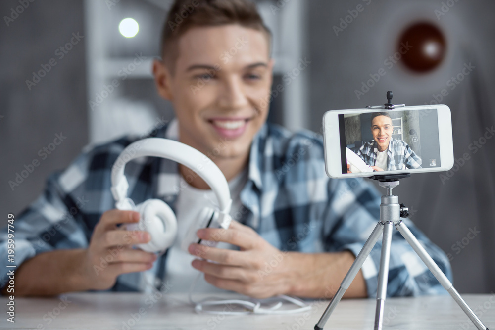 I love music. Nice happy successful well-built blogger holding his headphones and smiling while making a video I love music. Nice happy successful well-built blogger holding his headphones and smiling while making a video