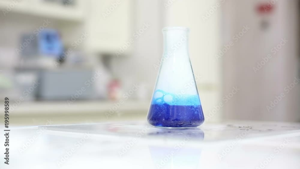 Cinemagraph of chemical reaction: blue liquid boiling in flask standing on laboratory bench, close-up shot