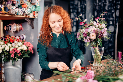 nice florist wearing black apron and green blouse collecting natural,coloful flowers,putting flowers into vase at florist's shop photo