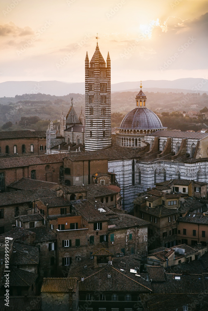 Picturesque backlit view of Siena Cathedral Santa Maria Assunta (Duomo) from Torre del Mangia tower at sunset golden hour, Tuscany, Italy. Scenic travel destiantion vertical postcard.