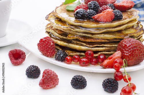 Delicious pancakes with berries and maple syrup on a white background