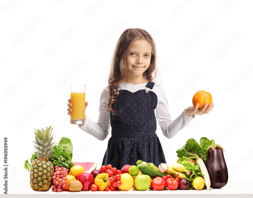 Girl holding a glass of juice and an orange behind a table with fruit and vegetables Girl holding a glass of juice and an orange behind a table with fruit and vegetables