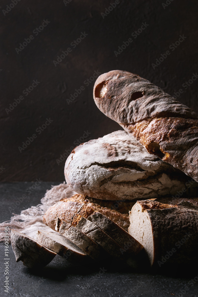 Obraz premium Variety of loafs fresh baked artisan rye and whole grain bread on linen cloth over dark brown texture background. Copy space.