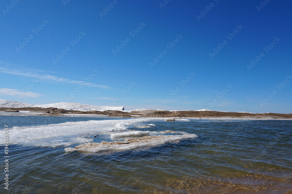 Edge of frozen Lake Michigan with icebergs in background and blue sky, ice floating in water