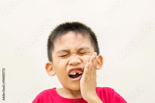 The boy is holding his hand on his cheek and red face with pain from toothache.