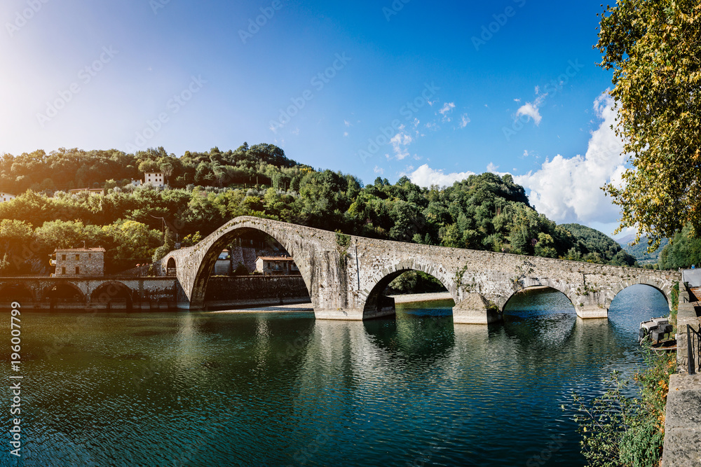 Picturesque view of medieval stone arch bridge Ponte della Maddalena across river Serchio in Borgo a Mozzano, Lucca, Tuscany, Italy. Scenic travel destination postcard.