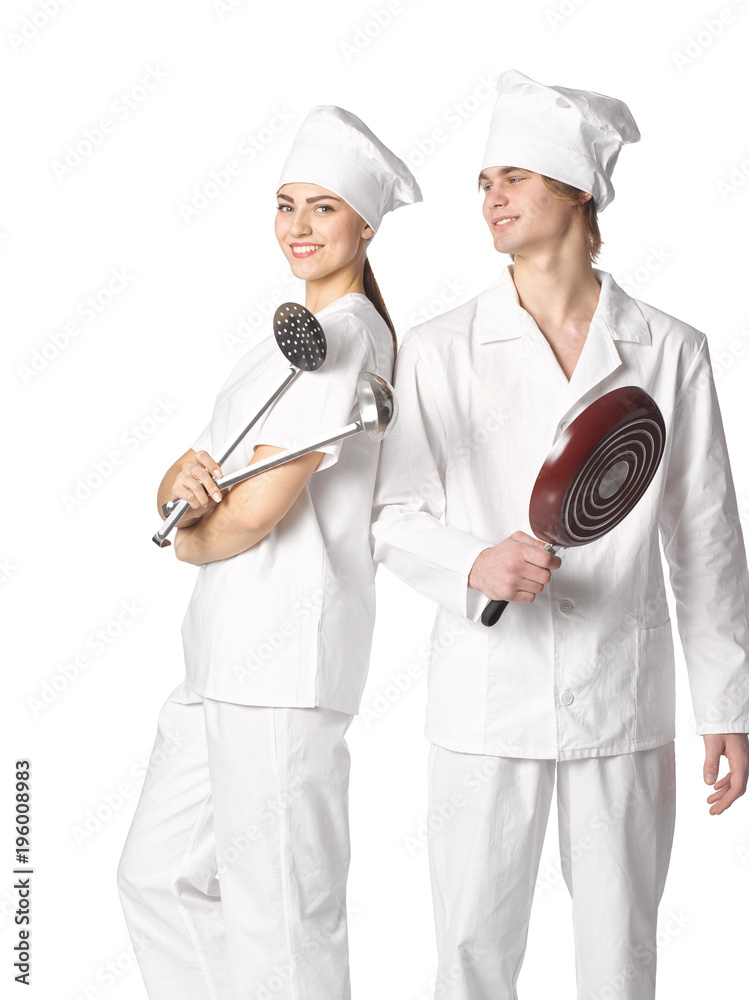 Beautiful young couple dressed in cooks with cooking tools standing side by side isolated on white background. Beautiful young couple dressed in cooks with cooking tools standing side by side isolated on white background.