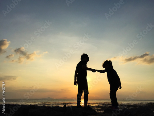 Silhouette of two sibling playing together at the beach on sunset