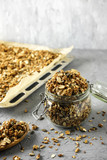 The process of storing homemade granola. A glass jar, a wooden spoon and a baking tray with a dry breakfast on the concrete background.