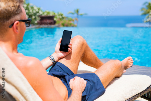 Man holding mobile phone while relaxing by the pool.